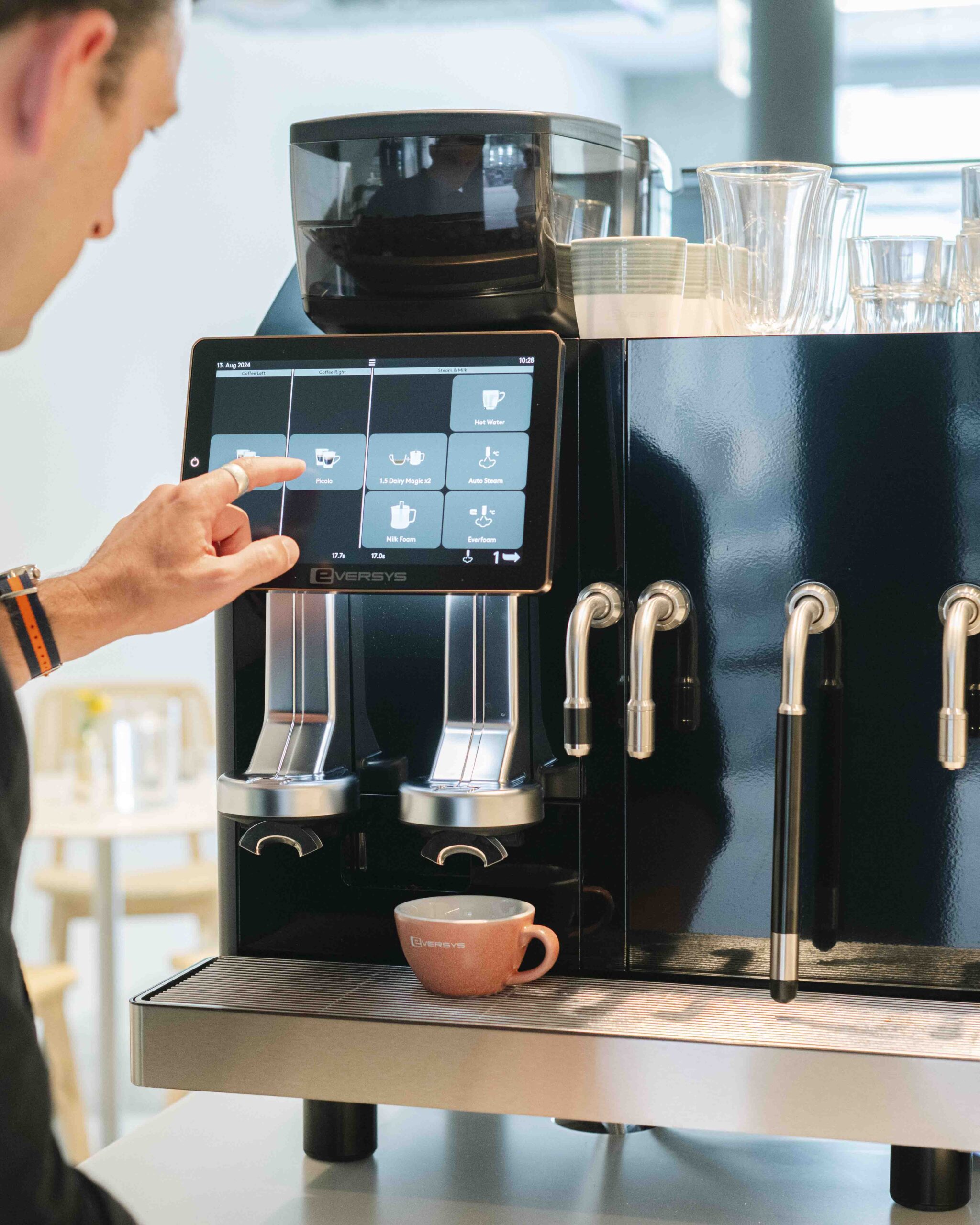 Mann bedient moderne Eversys-Kaffeemaschine über Touchscreen, Barista bereitet Kaffee zu
